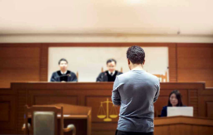 1049504825 Man stands in courtroom before judges and stenographer