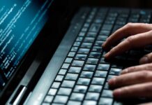 Close up of hands typing on a laptop keyboard with code displayed on the screen
