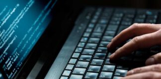 Close up of hands typing on a laptop keyboard with code displayed on the screen