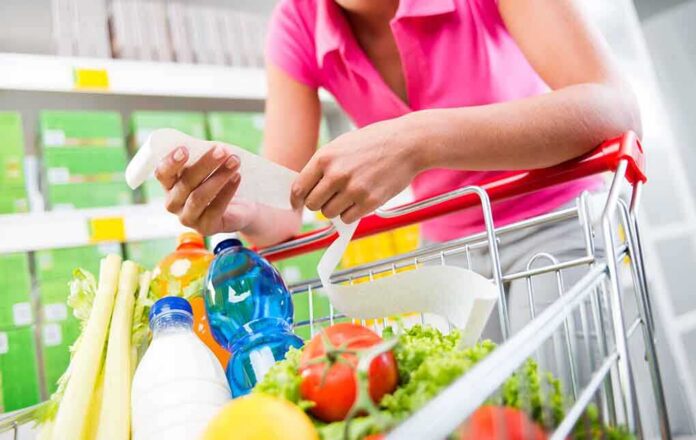Person holding a shopping list while looking at groceries in a cart