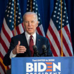 Man speaking at podium with American flags behind