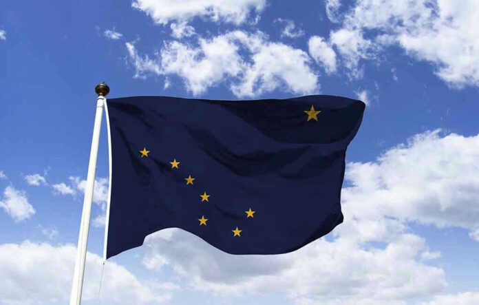 1363238492 Alaska state flag flying against a blue sky.