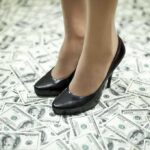 Congresswoman’s $5M Heist for Luxury Life A pair of black high heels standing on a floor covered with dollar bills