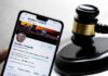 Smartphone displaying Twitter profile near a judges gavel.