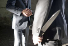 Two men shaking hands, one holding hidden knife.