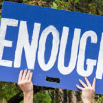 Person holding sign that says Enough outdoors