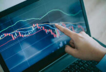 Hand pointing at stock market graph on laptop.