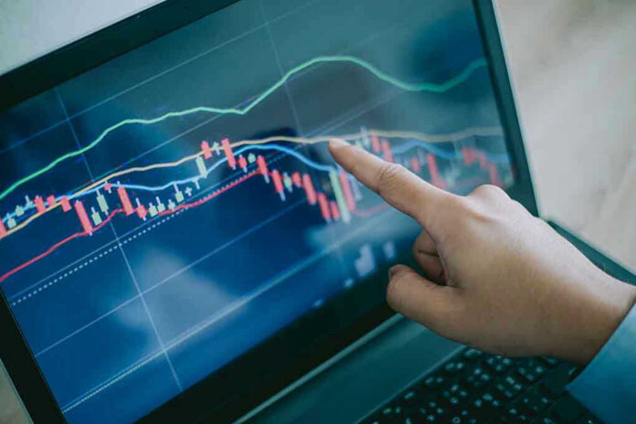 Hand pointing at stock market graph on laptop.