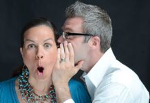 A surprised woman reacting while a man whispers in her ear