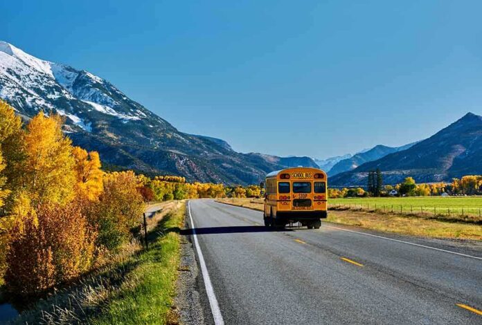 shutterstock_1151523266 (1).jpg A yellow school bus driving on a rural road surrounded by autumn trees and mountains