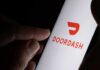 A hand holding a smartphone displaying the Doordash logo