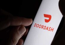 A hand holding a smartphone displaying the Doordash logo