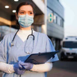 New Conflict Twist: Innocent Lives Lost Nurse in scrubs and mask outside hospital holding clipboard.