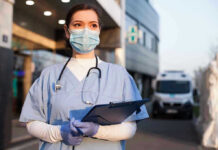 New Conflict Twist: Innocent Lives Lost Nurse in scrubs and mask outside hospital holding clipboard.