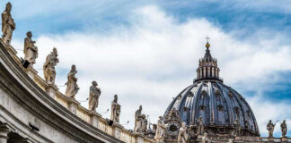 St. Peters Basilica dome with statues and clouds.