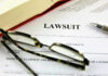 Lawsuit paperwork with glasses, pen, and an open book.