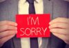 Judge APOLOGIZES to JAILED Assassin — Unthinkable! A man in a suit holding a red sign that says IM SORRY