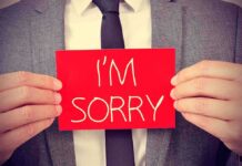 A man in a suit holding a red sign that says IM SORRY