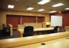 Public OUTRAGE Over Judge’s Domestic Violence RULING Interior view of an empty courtroom with wooden furniture and American flags