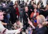 A crowded press conference with journalists and cameras surrounding a speaker