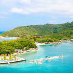Tropical beach with docks and lush green hills.