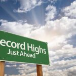 A green road sign indicating Record Highs Just Ahead against a cloudy sky