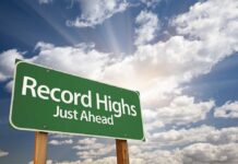 A green road sign indicating Record Highs Just Ahead against a cloudy sky