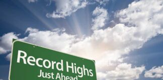 A green road sign indicating Record Highs Just Ahead against a cloudy sky