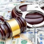 Judge's gavel and handcuffs on pile of US dollar bills