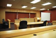 Interior view of an empty courtroom with wooden furniture and American flags