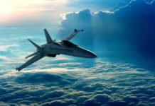 A fighter jet flying above the clouds during sunset