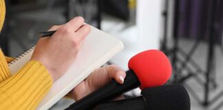 Journalist holding two microphones while writing in a notebook