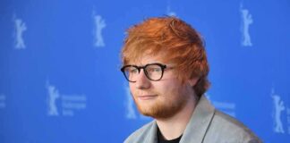 Ed Sheeran posing at a photo call against a blue backdrop