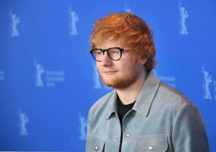 shutterstock_1035592693 Ed Sheeran posing at a photo call against a blue backdrop