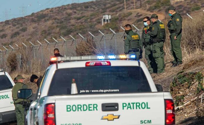 Border Patrol agents gather near fence with patrol trucks