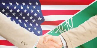 Handshake between two people over U.S. and Saudi flags