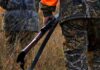 Hunter in camouflage holding a rifle in tall grass