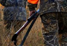 Hunter in camouflage holding a rifle in tall grass
