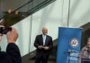Man in a suit at a public event near a blue banner