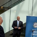 Man in a suit at a public event near a blue banner