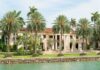 Waterfront mansion with palm trees and grand columns