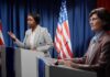 Two women at podiums during a debate with U.S. flags behind them