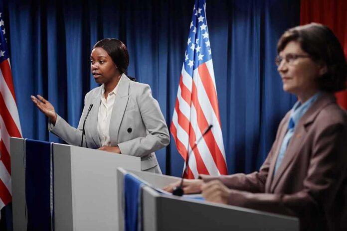 Two women at podiums during a debate with U.S. flags behind them
